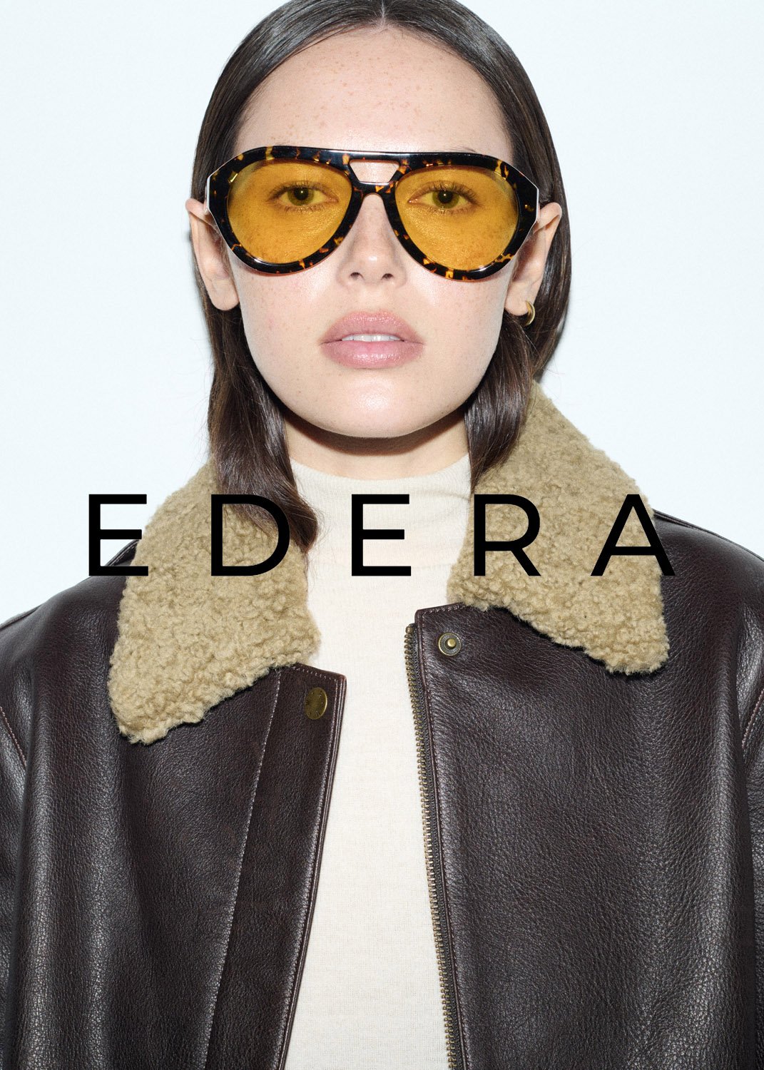 Woman with brown hair, wearing a leather jacket and glasses, posing against a white background, featuring the 'EDERA' brand.
