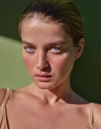 Close up beauty portrait of a woman with slicked back hair and freckles against a green background