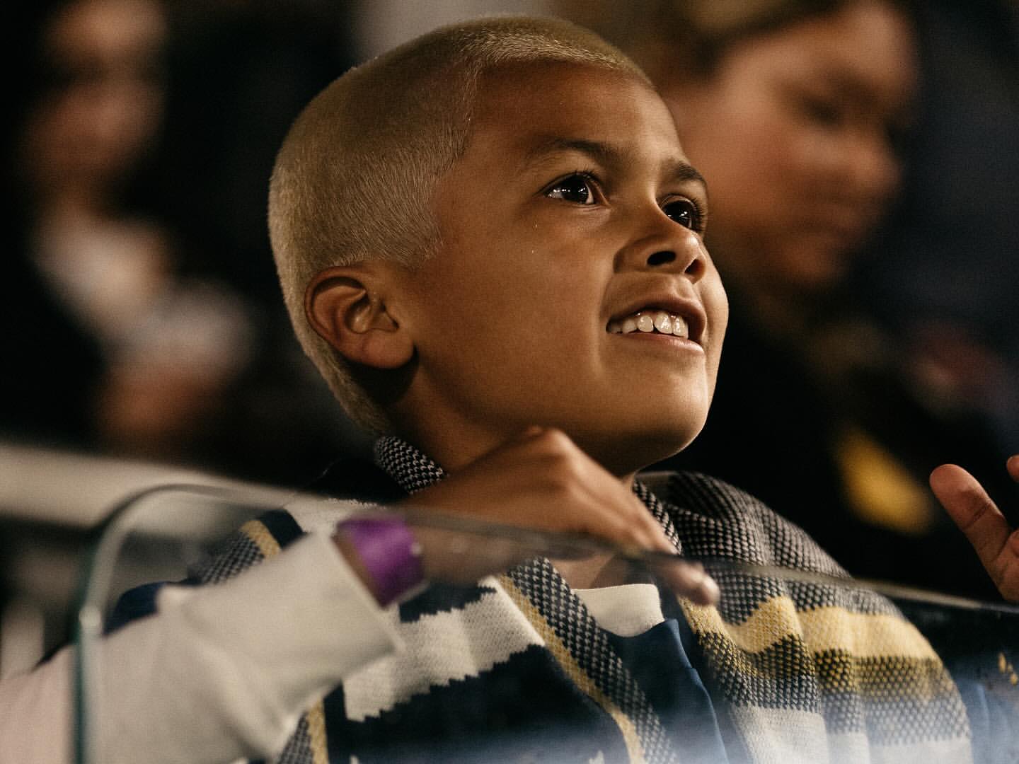 Young child with short blonde hair and striped scarf looking upward smiling, photographed by Hana Asano in New York.