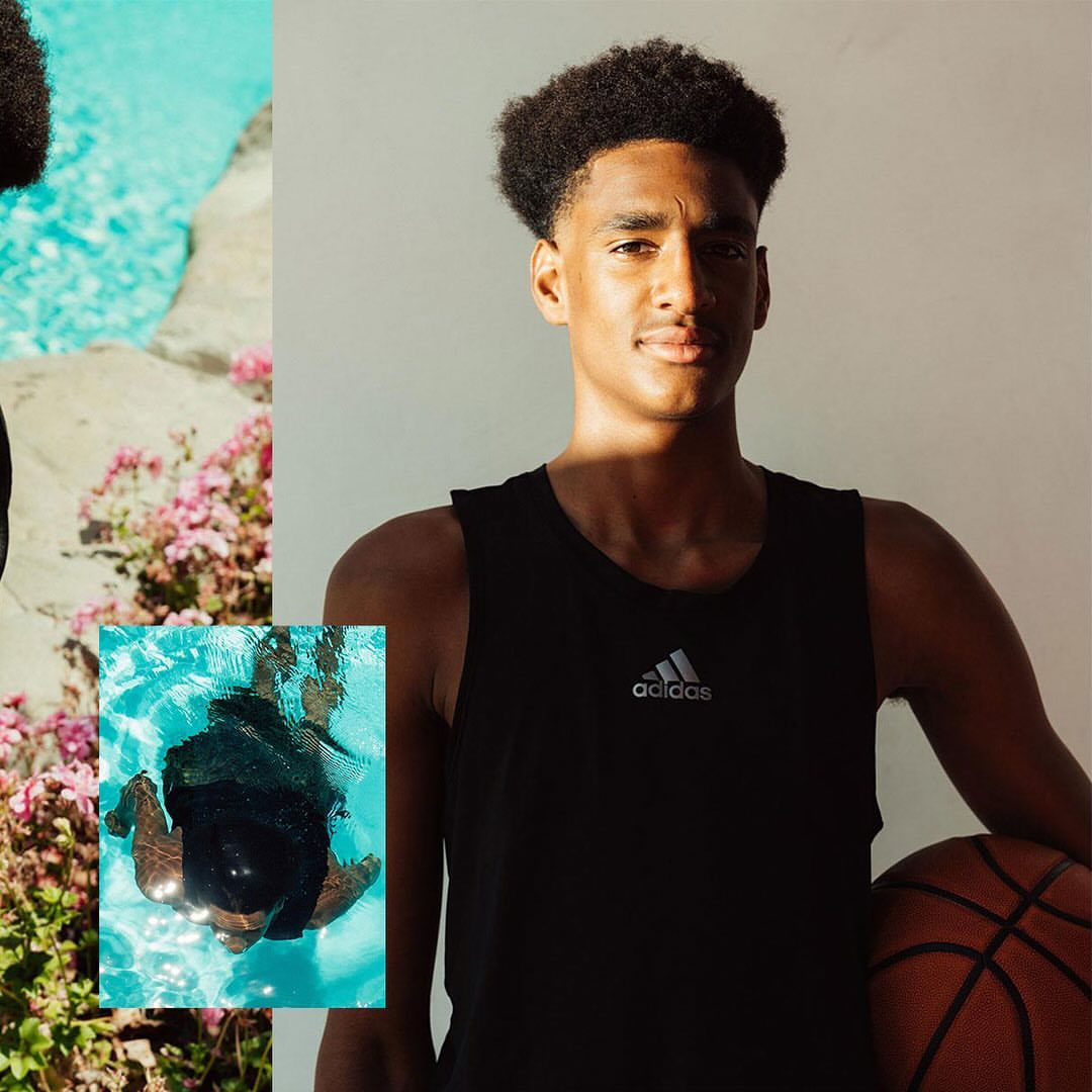 Portrait of a young adult male in a black tank top holding a basketball, with a pool and flowers in the background.