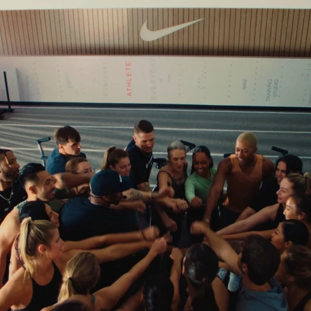 Group of diverse athletes in a huddle with hands together in a gym setting under the Nike logo. Teamwork and unity in sports.