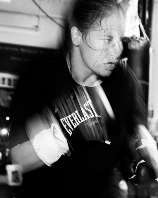 Female boxer training in gym, wearing Everlast shirt and boxing gloves. Black and white action shot with motion blur and close up framing.