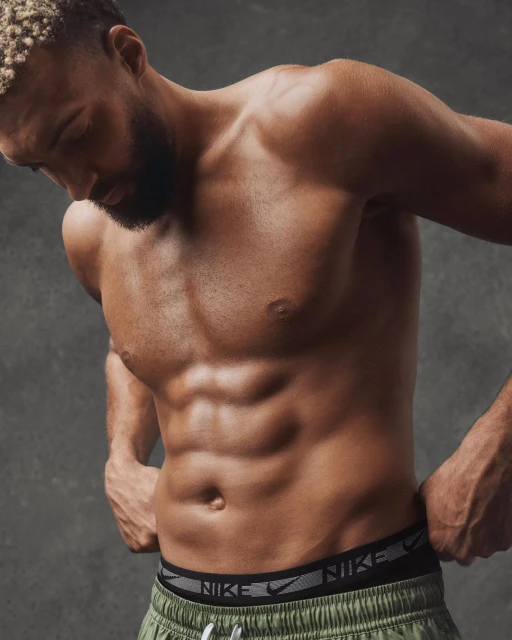 Athletic adult male showing muscular physique in a studio shot, wearing green athletic shorts with the Nike logo on the waistband.