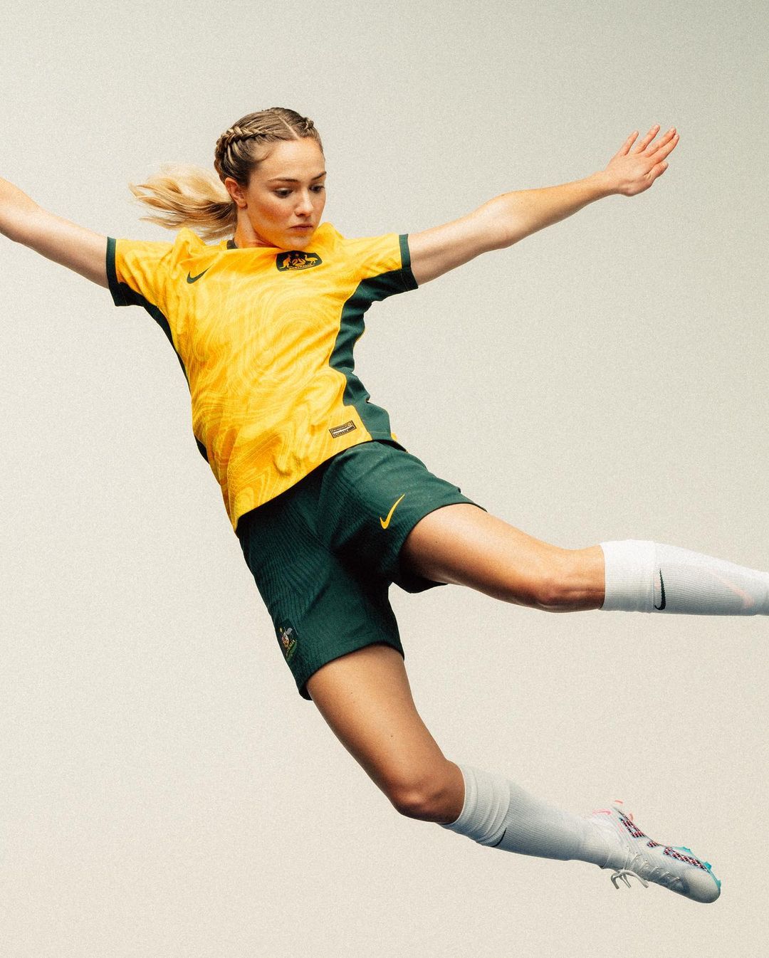Athlete in action wearing a yellow and green Australia soccer uniform against a bright studio background, showcasing dynamic movement.