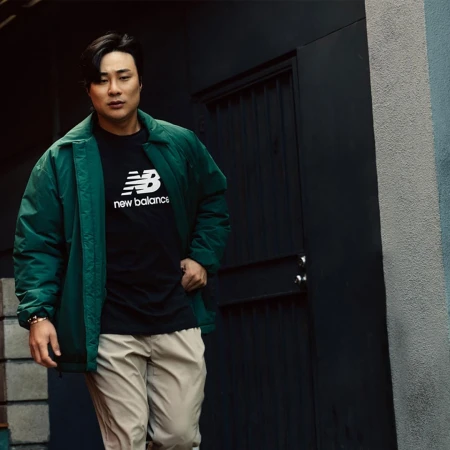 Asian male model in green jacket and khakis poses in front of a black metal door with silver hardware, urban background, natural light.