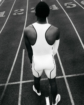 Back view of a Black male athlete in a white uniform on a running track, focused on the start line with lane numbers, monochrome.