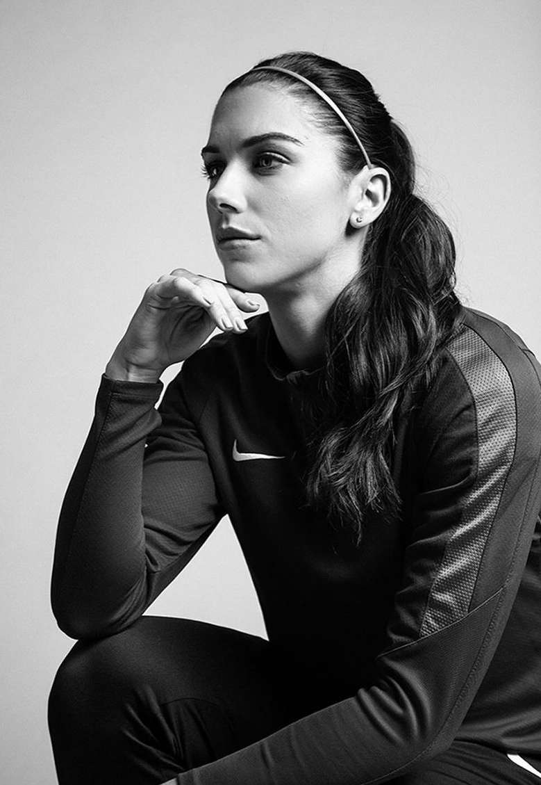 Monochrome portrait of a woman in athletic wear with a headband, seated with her hand to her face in a contemplative pose.