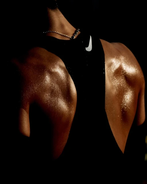Close-up shot of an adult male's back and shoulders with visible musculature and perspiration, wearing a black tank top with the Nike logo.