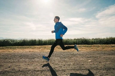 A man in a blue running jacket and black tights runs along a dirt path under an open sky photographed by Hana Asano.