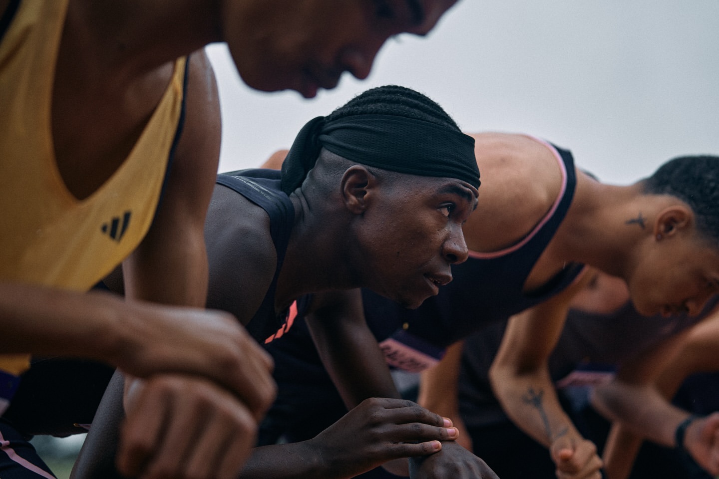 Close-up shot of athletes lined up in starting positions, wearing sports gear and headbands, focus on the athlete in the foreground.
