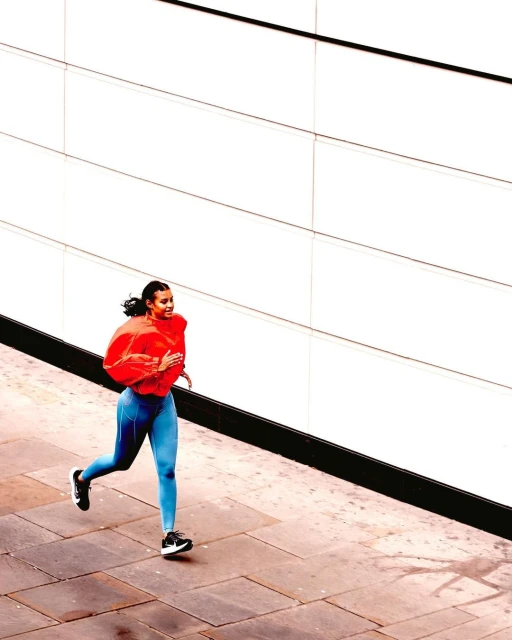 A woman in workout gear running on a city sidewalk next to a modern building with white facade and black trim, full-length shot.