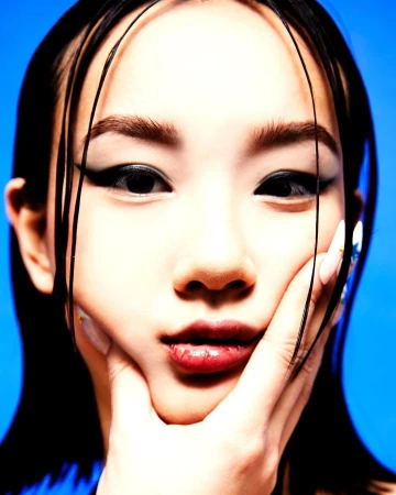 Close-up portrait of a woman with wet dark hair and winged eyeliner holding her cheek against a vibrant blue background.
