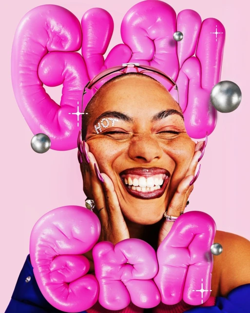 Woman with pink balloon letters spelling 'Glam,' smiling with her eyes closed, wearing sunglasses and showing long acrylic nails.
