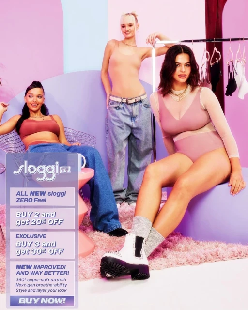 Three women pose indoors wearing lingerie and casual wear in a studio setting with a lilac color scheme and Sloggi ad.
