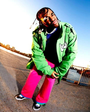Man wearing a bright green jacket and hot pink trousers posing outdoors against a clear sky background in London by photographer Hanina.