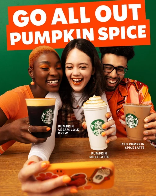 Three smiling friends pose for a selfie with Starbucks Pumpkin Spice beverages against a green backdrop, promoting the seasonal menu.