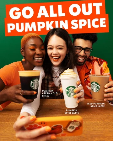 Three smiling friends pose for a selfie with Starbucks Pumpkin Spice beverages against a green backdrop, promoting the seasonal menu.