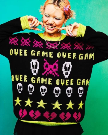 Smiling woman wearing a black knitted sweater with video game pixel art-style graphics, with bright pink and neon yellow details.