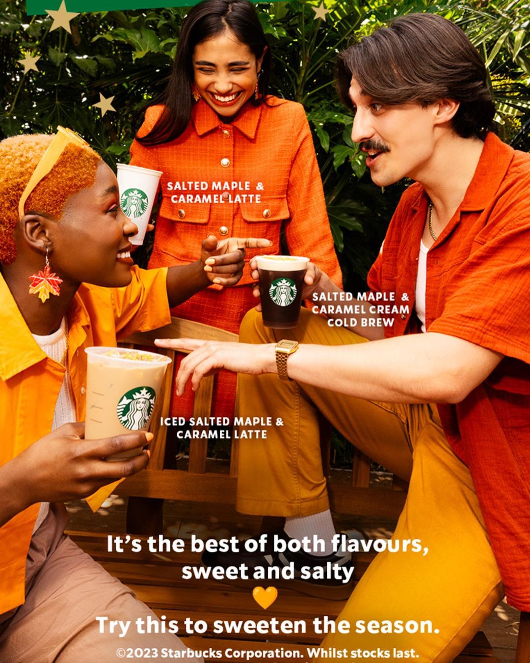 Three people of mixed ethnicities smile while holding Starbucks salted maple and caramel lattes in an outdoor, daytime setting.