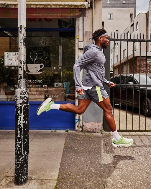 Athletic man running outdoors on an urban sidewalk near a storefront in athletic wear and neon green running shoes demonstrating fitness.