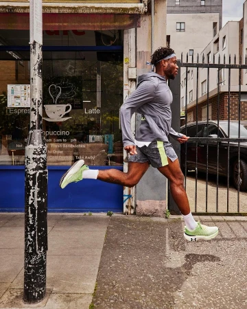 Athletic man running outdoors on an urban sidewalk near a storefront in athletic wear and neon green running shoes demonstrating fitness.