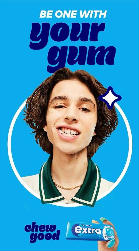 Close-up studio shot of a young adult male smiling with a pack of Extra gum in his hand on a bright blue background.