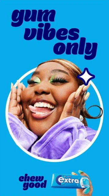 Woman with dark skin and green eye makeup, smiling and holding her hands on either side of her face; Extra gum in the foreground.