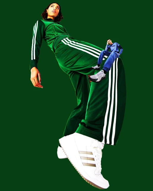 Woman poses in green Adidas tracksuit with giant shoe. A miniature man in a blue suit sits on the pant leg in this fashion collage.