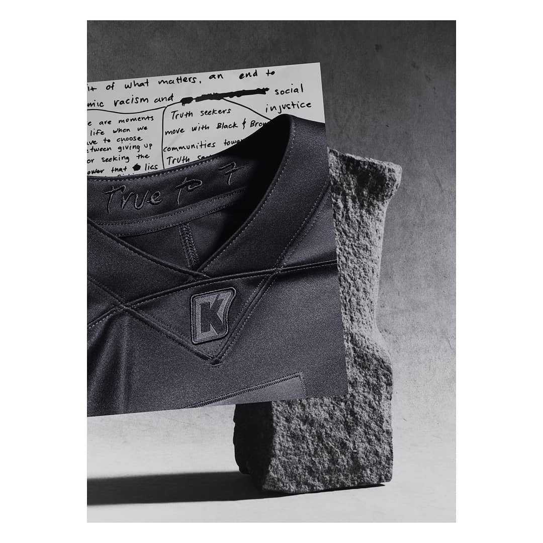 Abstract still life with a black jersey featuring a logo, juxtaposed with a handwritten note and a textured rock fragment.