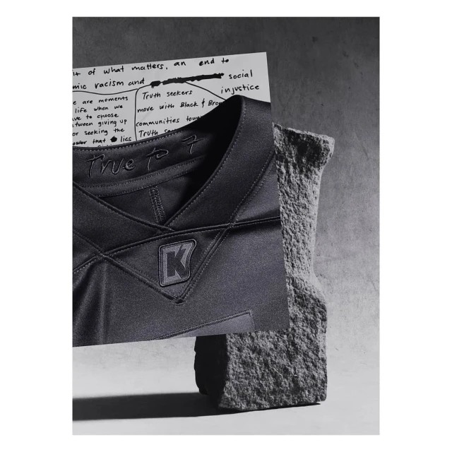 Abstract still life with a black jersey featuring a logo, juxtaposed with a handwritten note and a textured rock fragment.