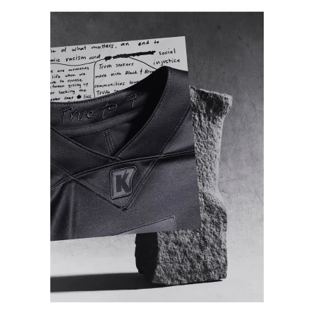 Abstract still life with a black jersey featuring a logo, juxtaposed with a handwritten note and a textured rock fragment.