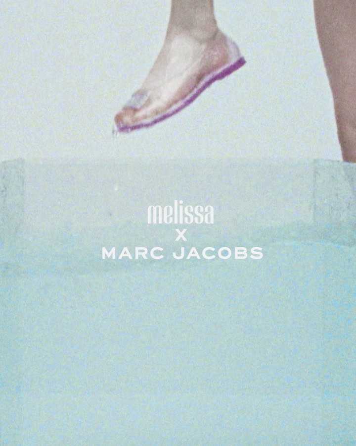 Foot with pink sandal above a bright blue surface, with Melissa x Marc Jacobs branding. Fashion forward shoe advertisement.