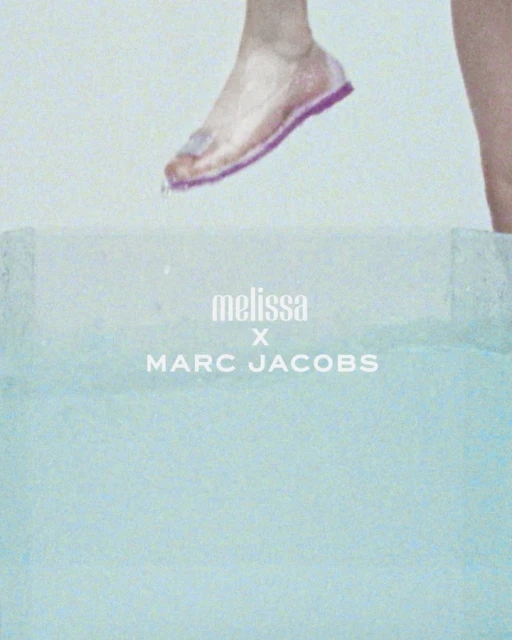 Foot with pink sandal above a bright blue surface, with Melissa x Marc Jacobs branding. Fashion forward shoe advertisement.