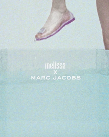 Foot with pink sandal above a bright blue surface, with Melissa x Marc Jacobs branding. Fashion forward shoe advertisement.