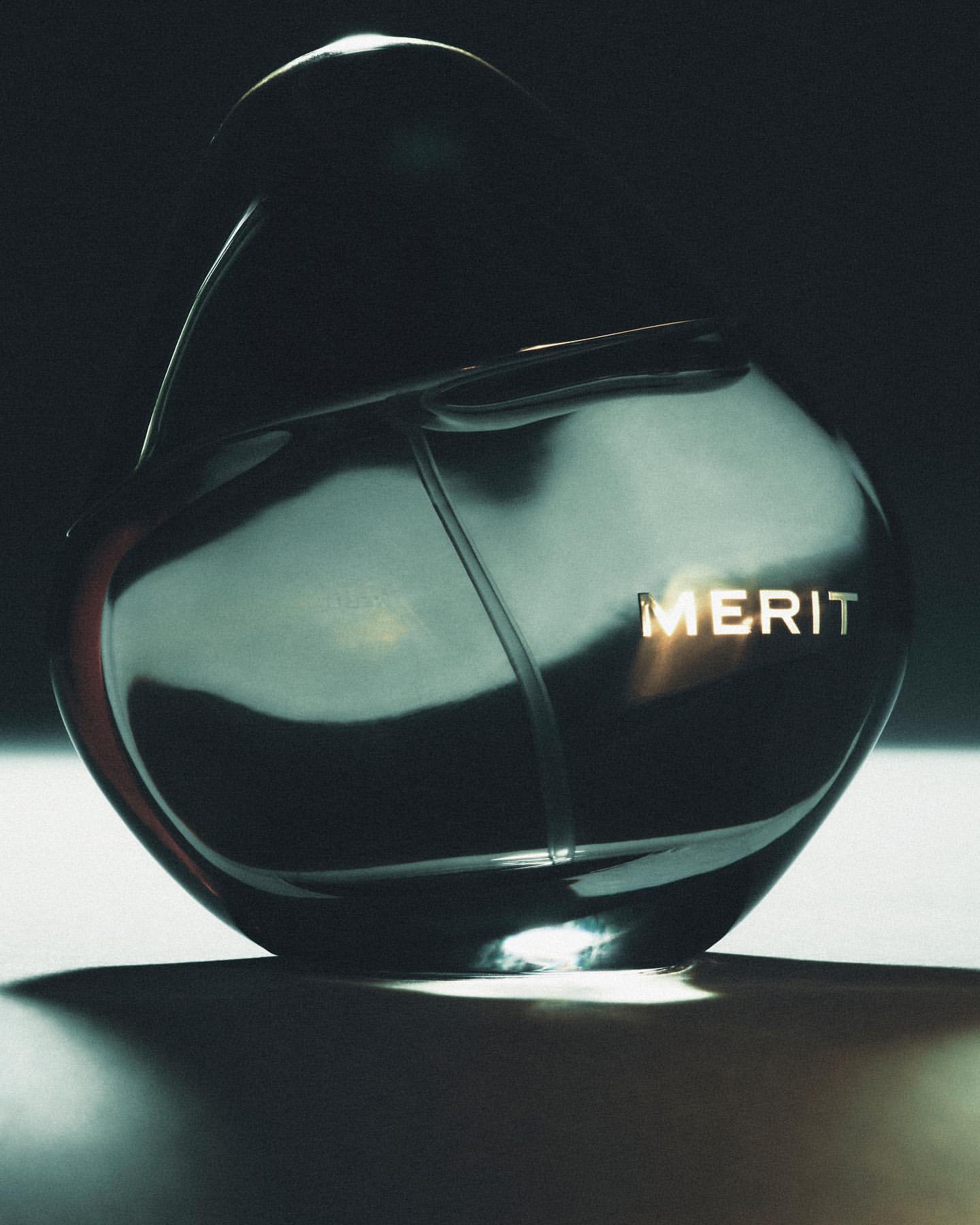 Elegant still life of a reflective glass perfume bottle with a gold label on a neutral surface, bathed in soft, indirect lighting.