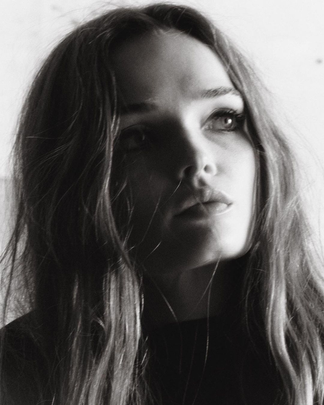 Close-up monochrome portrait of a woman with long hair looking upward in natural light by photographer Hanna Tveite.
