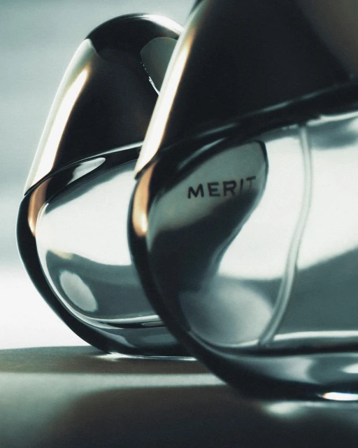 Close-up of two sleek, reflective perfume bottles with black accents and the word 'MERIT' visible, set against a soft gradient backdrop.