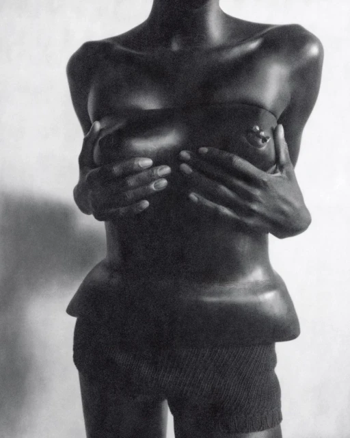 Monochrome studio shot of an African-descent woman covering her breasts with her hands, wearing high-waisted shorts against a white background.