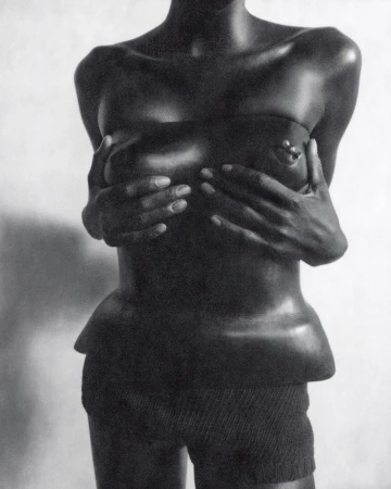 Monochrome studio shot of an African-descent woman covering her breasts with her hands, wearing high-waisted shorts against a white background.