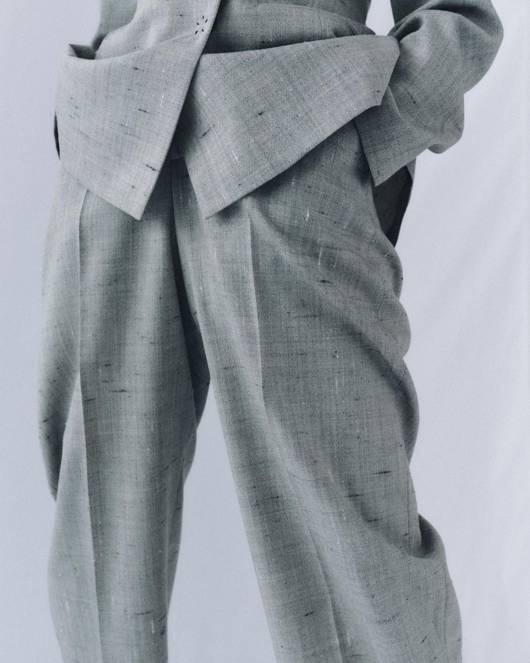 Grey textured suit with structured design and straight leg pants. The suit is presented on a white backdrop, focusing on fabric details.
