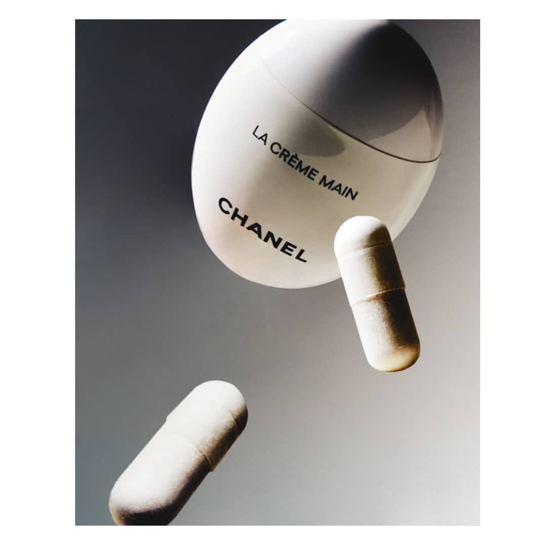 Cosmetic still life featuring a white cream bottle with the Chanel logo and two cosmetic capsules against a gradated grey background.