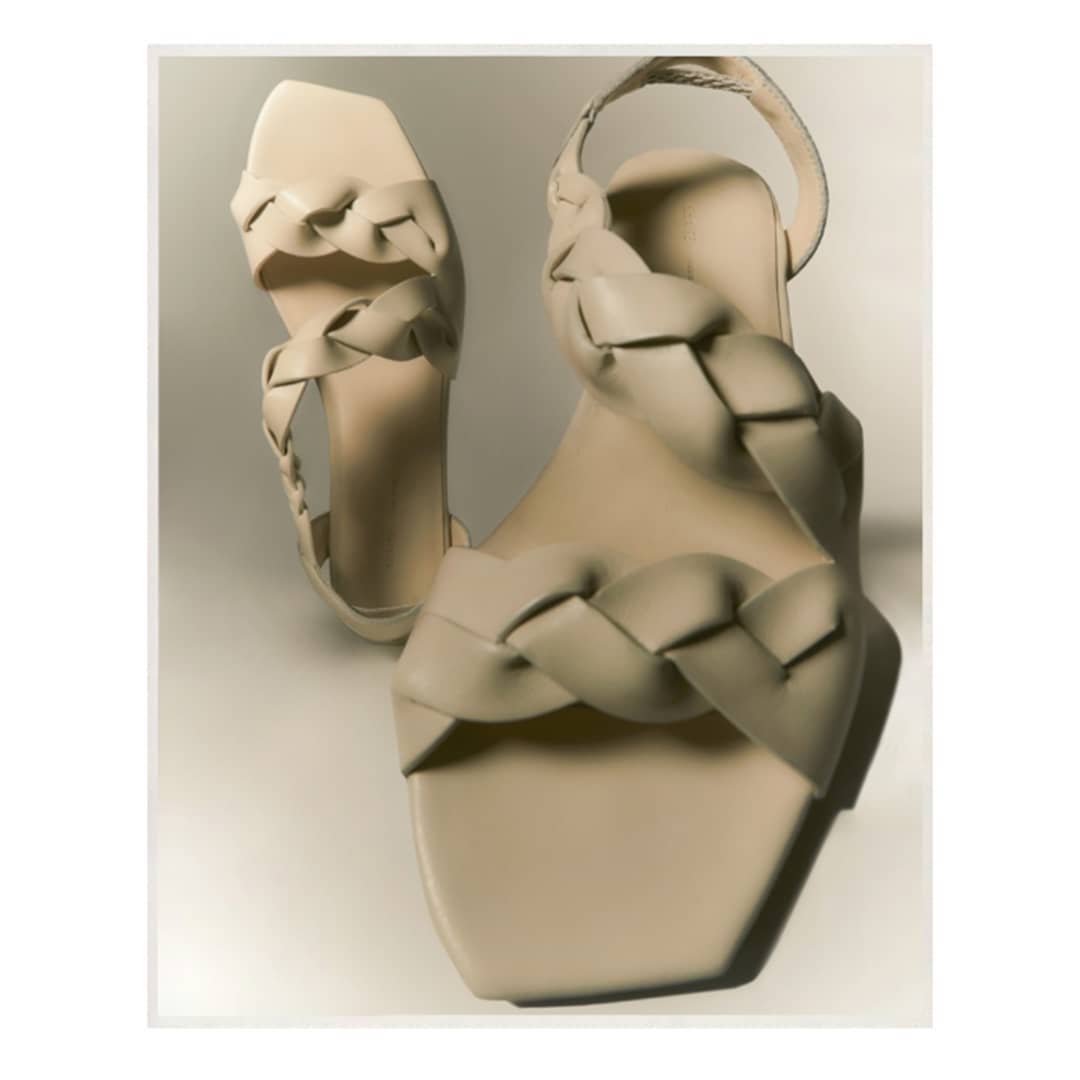 Cream woven heeled sandals are displayed on a cream background. The sandals feature a square toe and a delicate ankle strap.