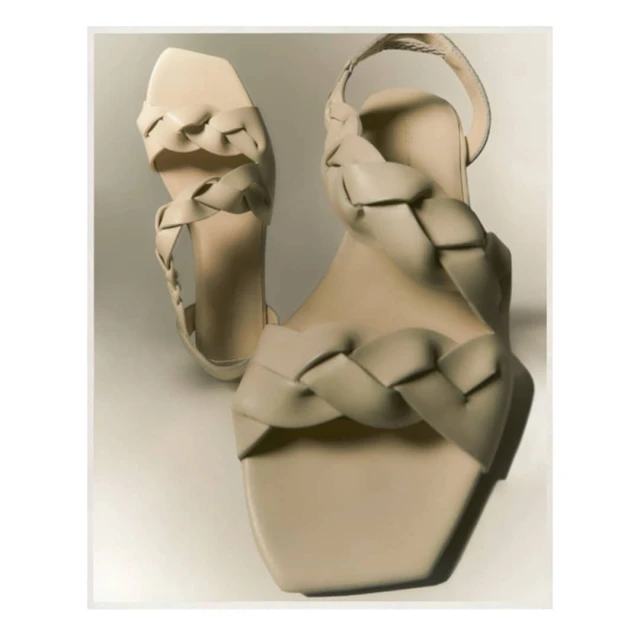 Cream woven heeled sandals are displayed on a cream background. The sandals feature a square toe and a delicate ankle strap.