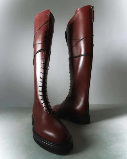 Pair of knee-high, lace-up maroon leather boots with a platform sole, set against a gradient grey background in a fashion product shot.