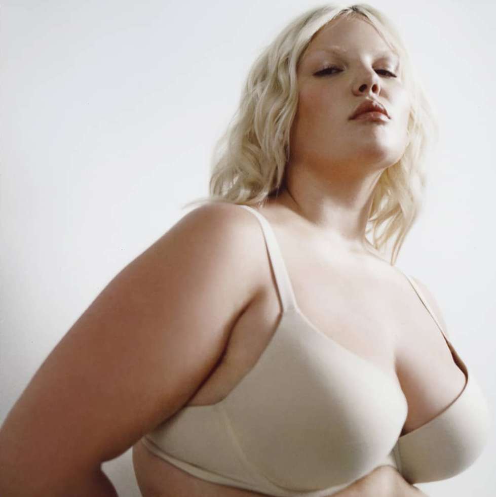 Portrait of a plus-size adult female in a bra against a white background, showcasing body positivity and self-love in a studio setting.