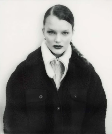 Monochromatic portrait of a woman with slicked-back hair wearing a black, buttoned jacket and a white top, set against a white background.