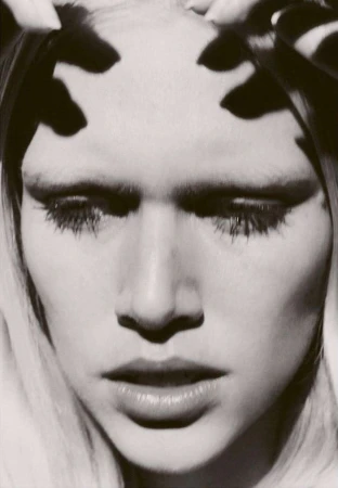Close up portrait of a woman with dramatic black shadows cast across her forehead by fingers, photographed by Hanna Tveite.