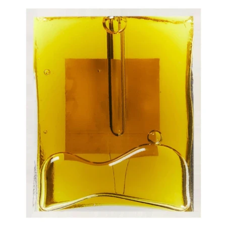 Abstract close-up of a block of transparent amber material with rounded shapes and a small, gold square embedded in the center.