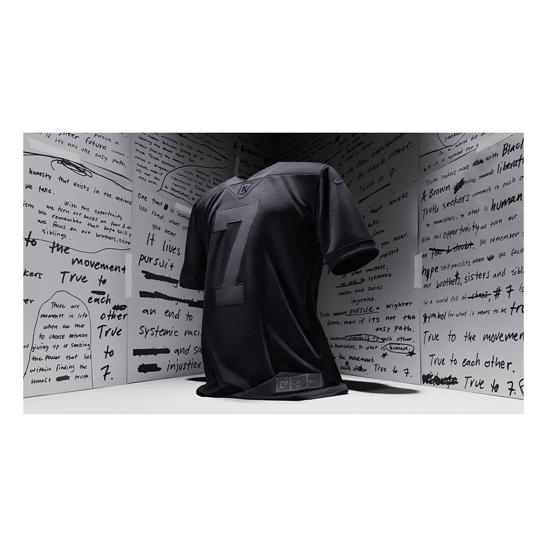 Black jersey with the number seven on display against a backdrop of white panels covered in handwritten text. Minimalist presentation.