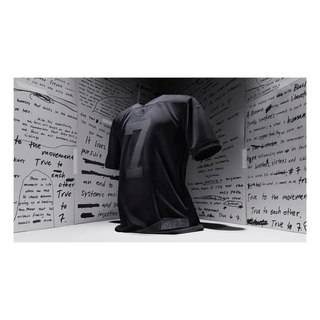 Black jersey with the number seven on display against a backdrop of white panels covered in handwritten text. Minimalist presentation.